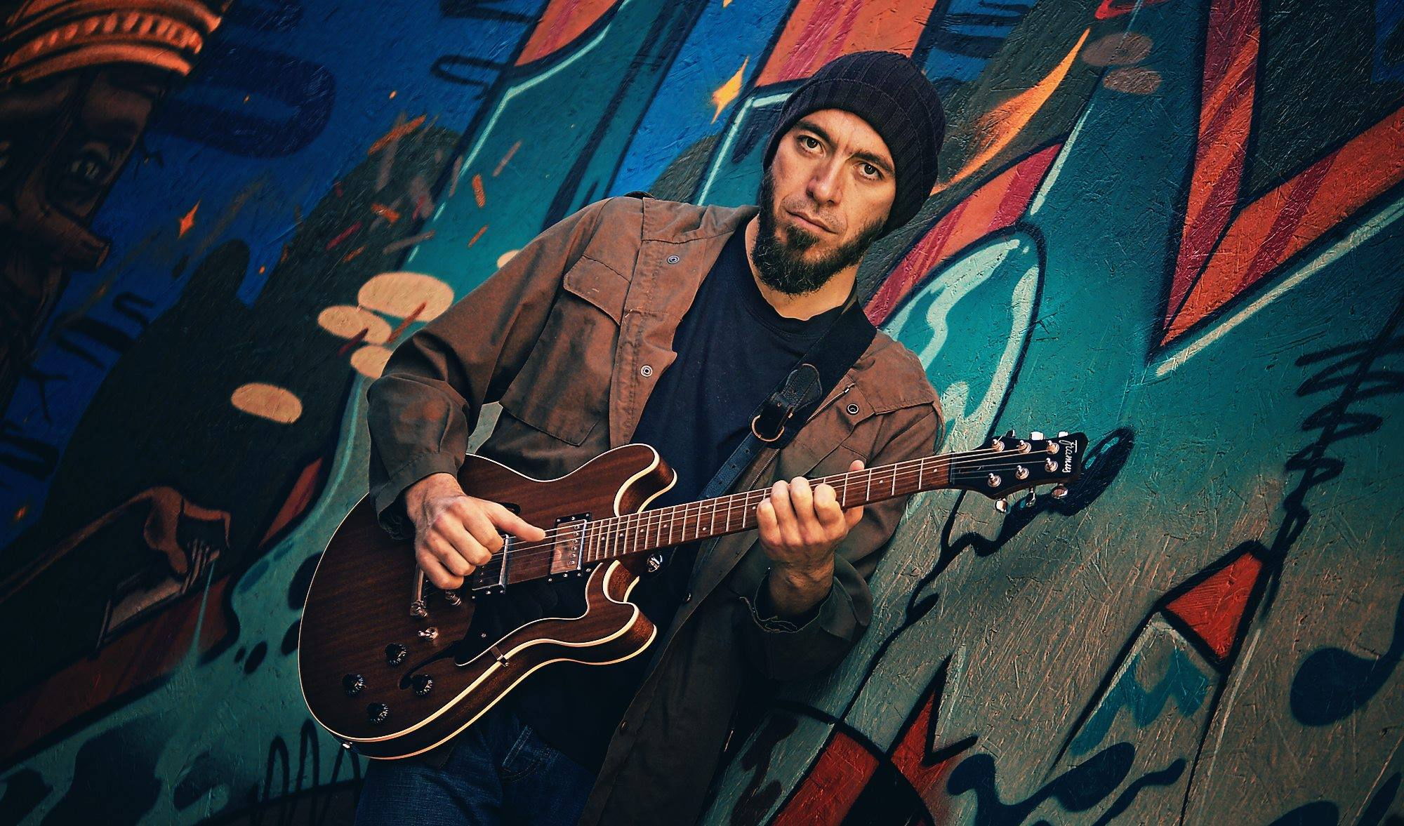 Cyfer with guitar against graffiti wall